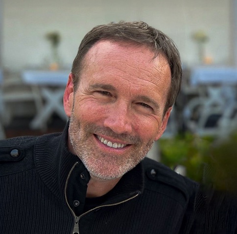 Smiling man outdoors in casual attire.